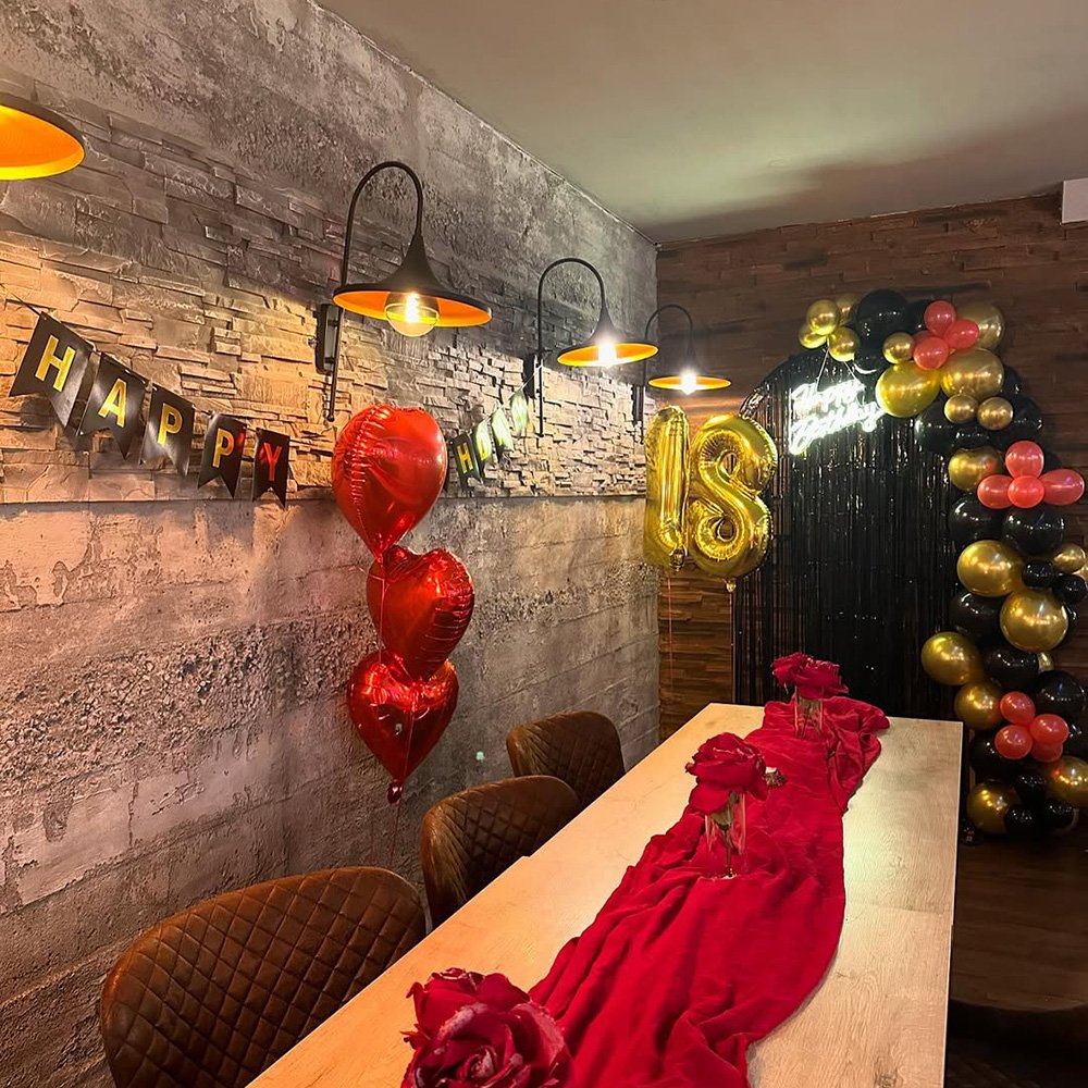 Dekoration einer Geburtstagsfeier mit roten und goldenen Ballons sowie einem langen Tisch mit rotem Stoffläufer.