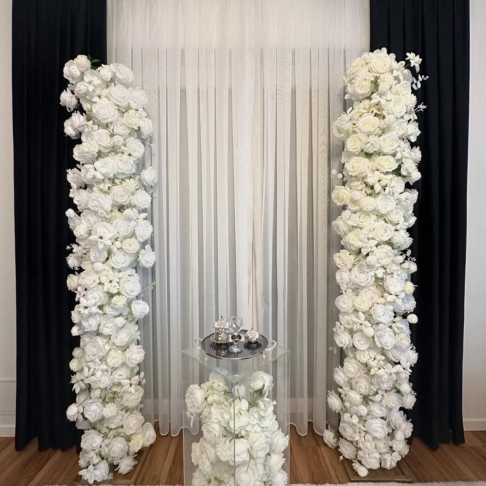 Weiße Blumensäulen flankieren einen transparenten Tisch mit eleganter Dekoration.