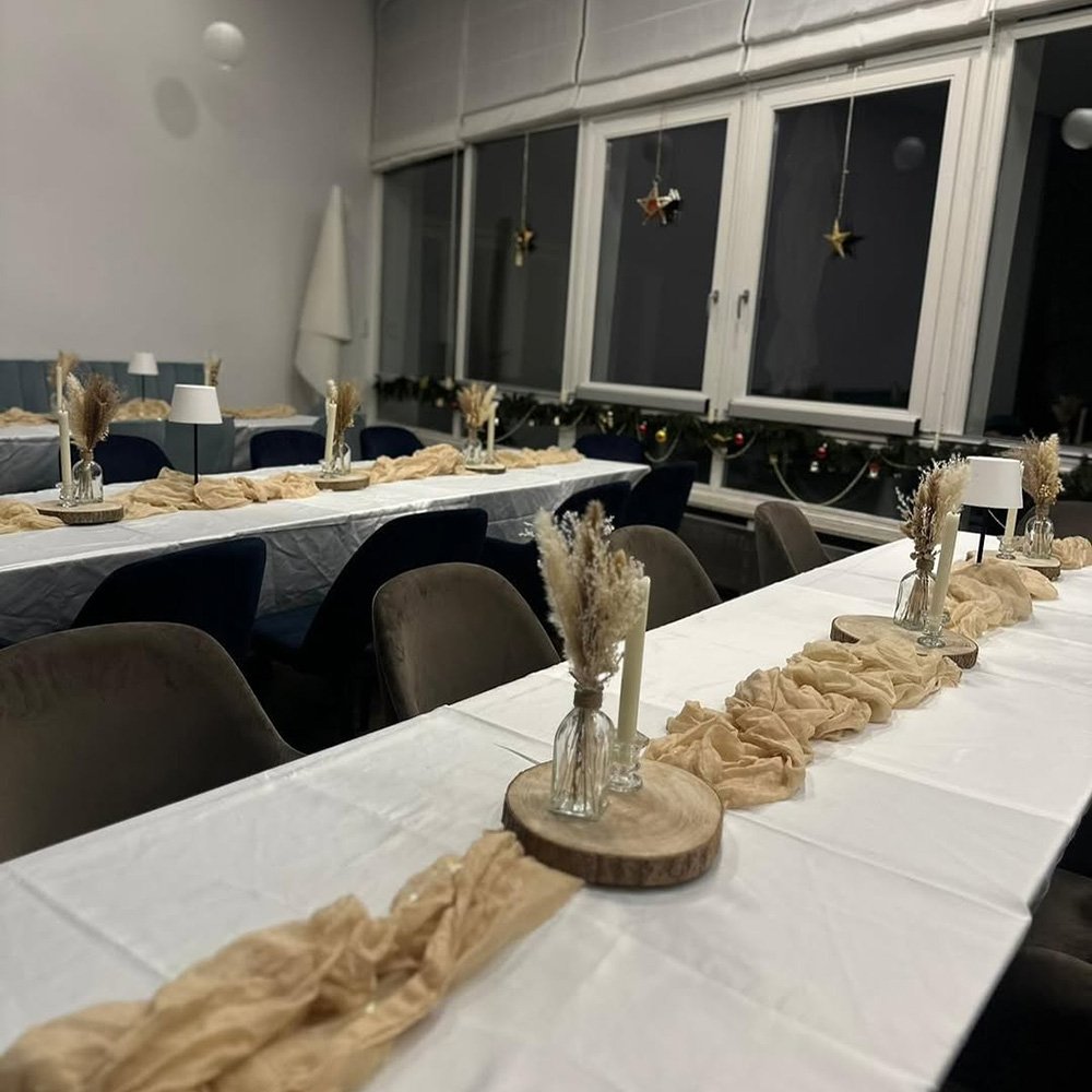 Lange Tische mit beiger Tischläufer-Dekoration und kleinen Vasen mit Trockenblumen.